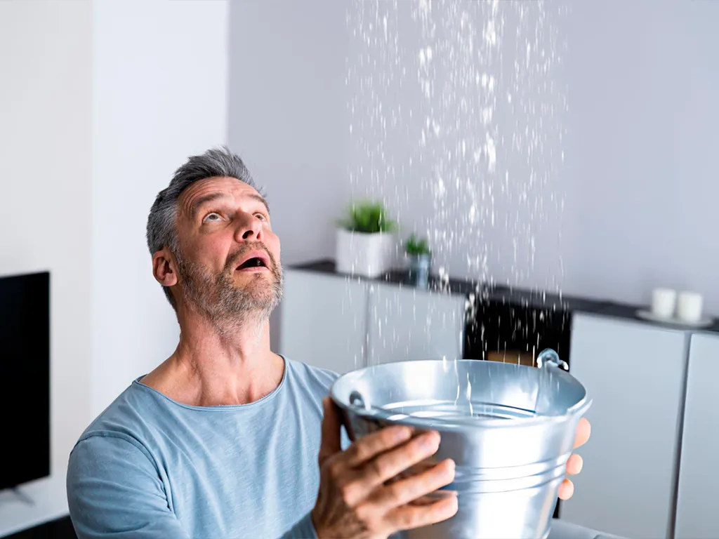 homem com balde na mão com goteira devido a vazamento de água